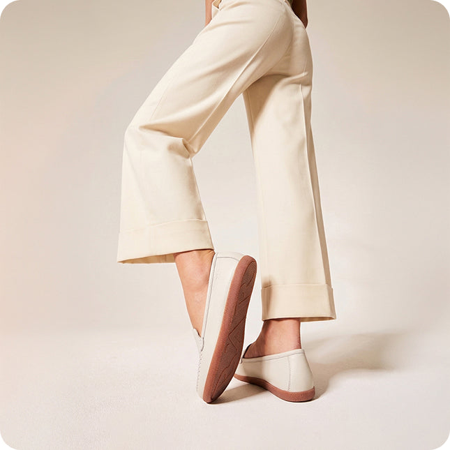 White shoes with brown soles worn with beige pants on a light background
