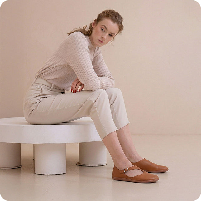 Woman sitting on a white bench wearing a beige outfit and brown shoes