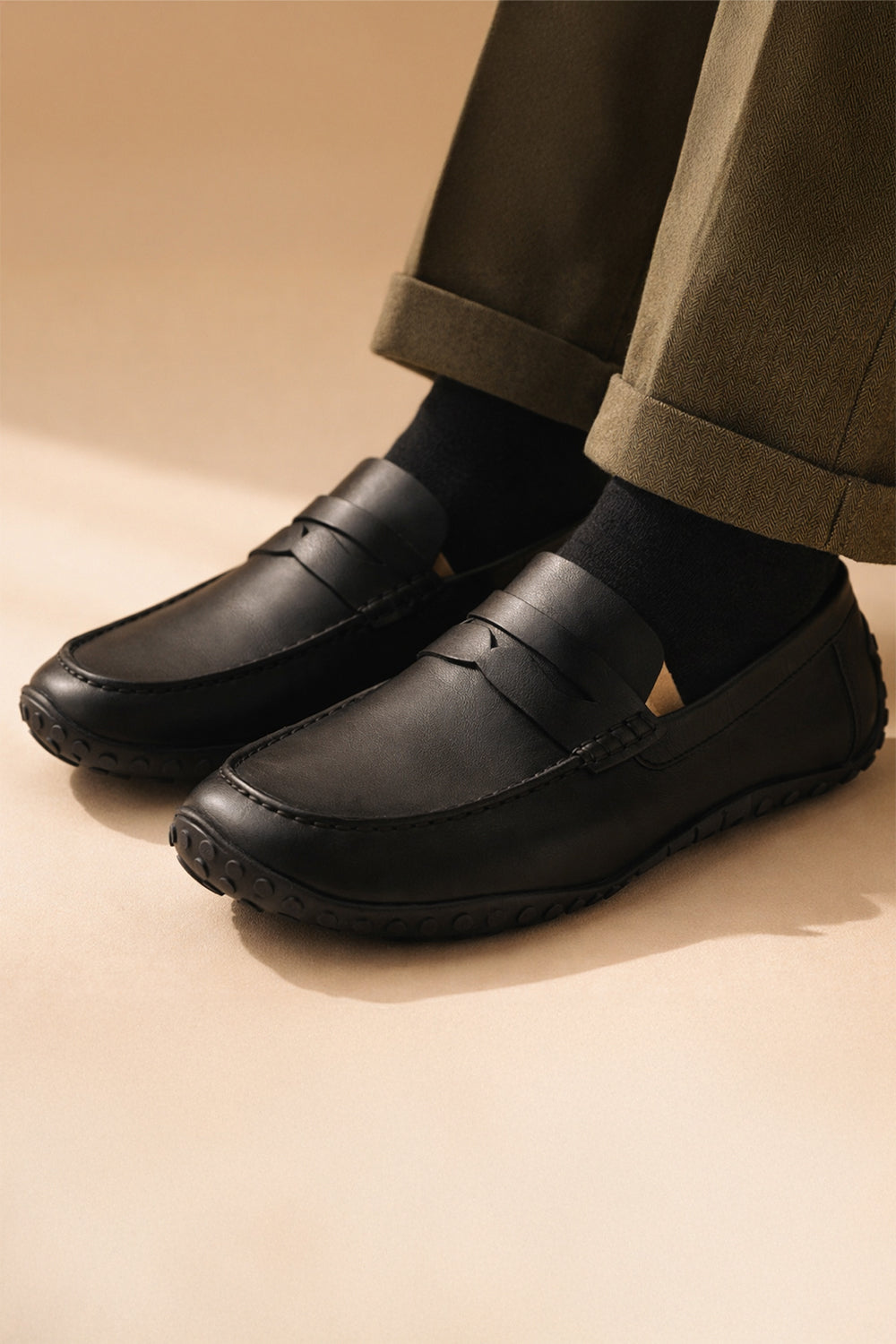 Black loafers worn with beige pants on a beige background
