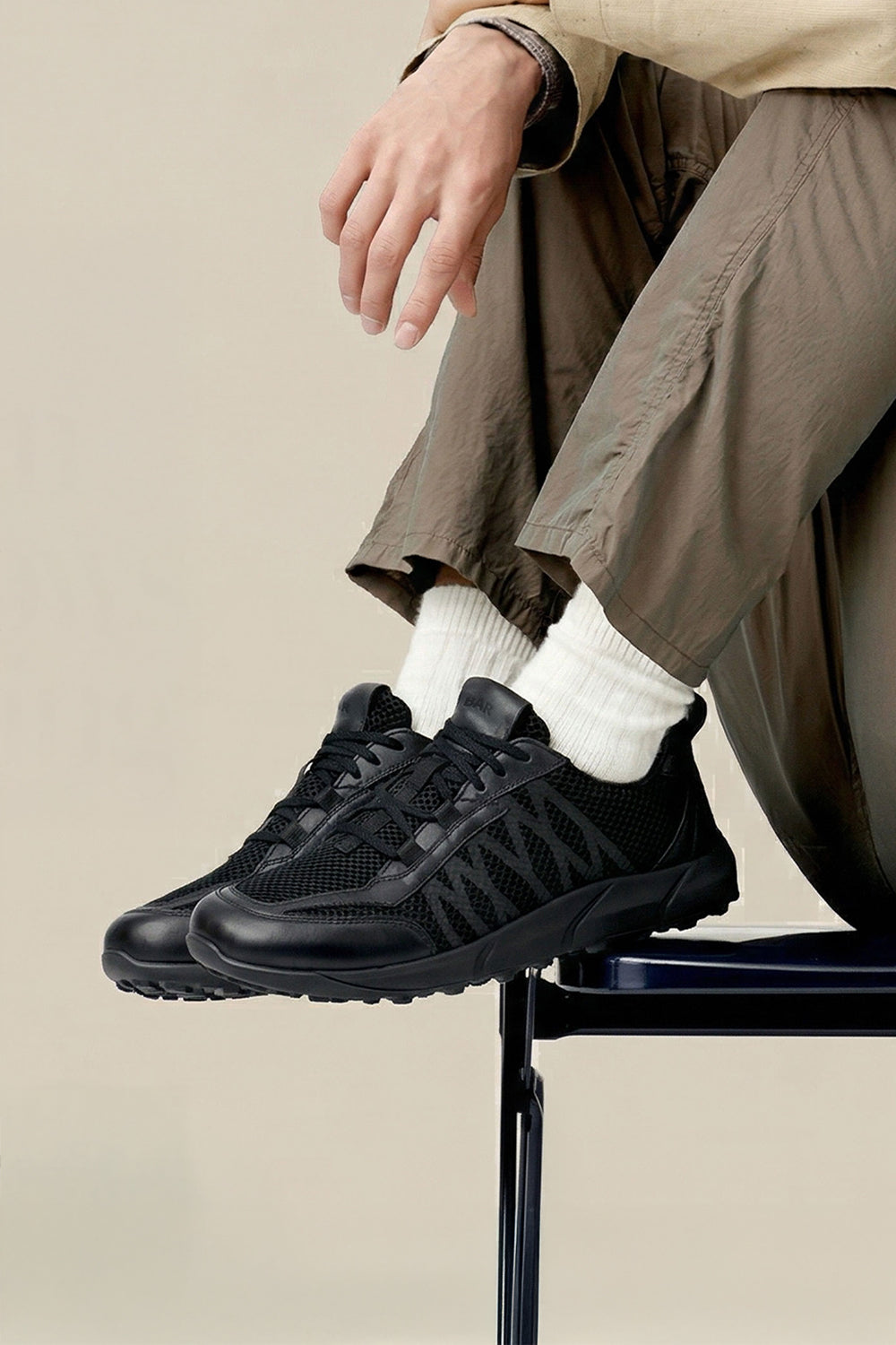 Person wearing black sneakers with white socks on a beige background