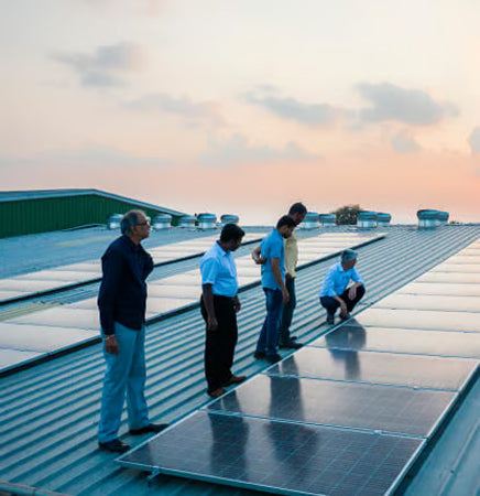 Group of people on a rooftop inspecting solar panels with a sunset sky.