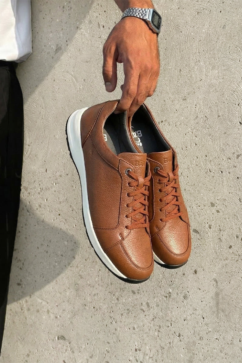 Brown leather sneakers with white soles on a concrete surface