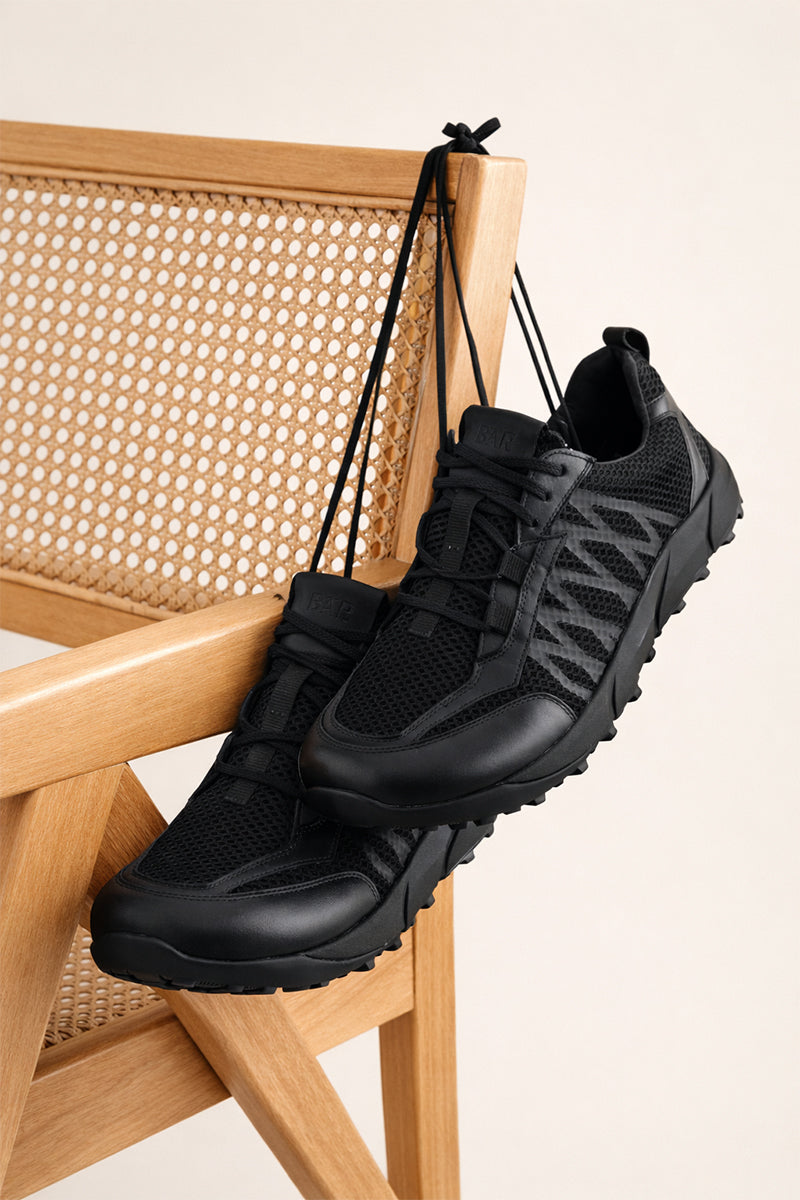 Black athletic shoes hanging on a wooden chair with a beige background
