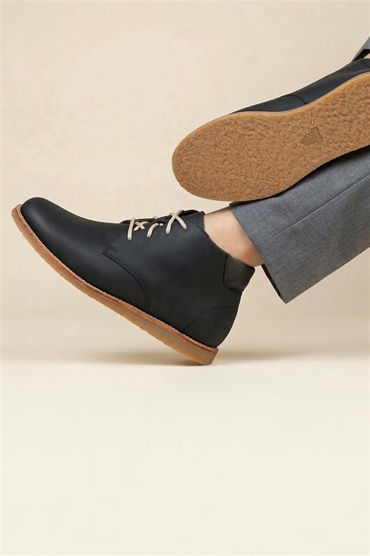 Black leather shoes with brown soles worn by a person on a beige background